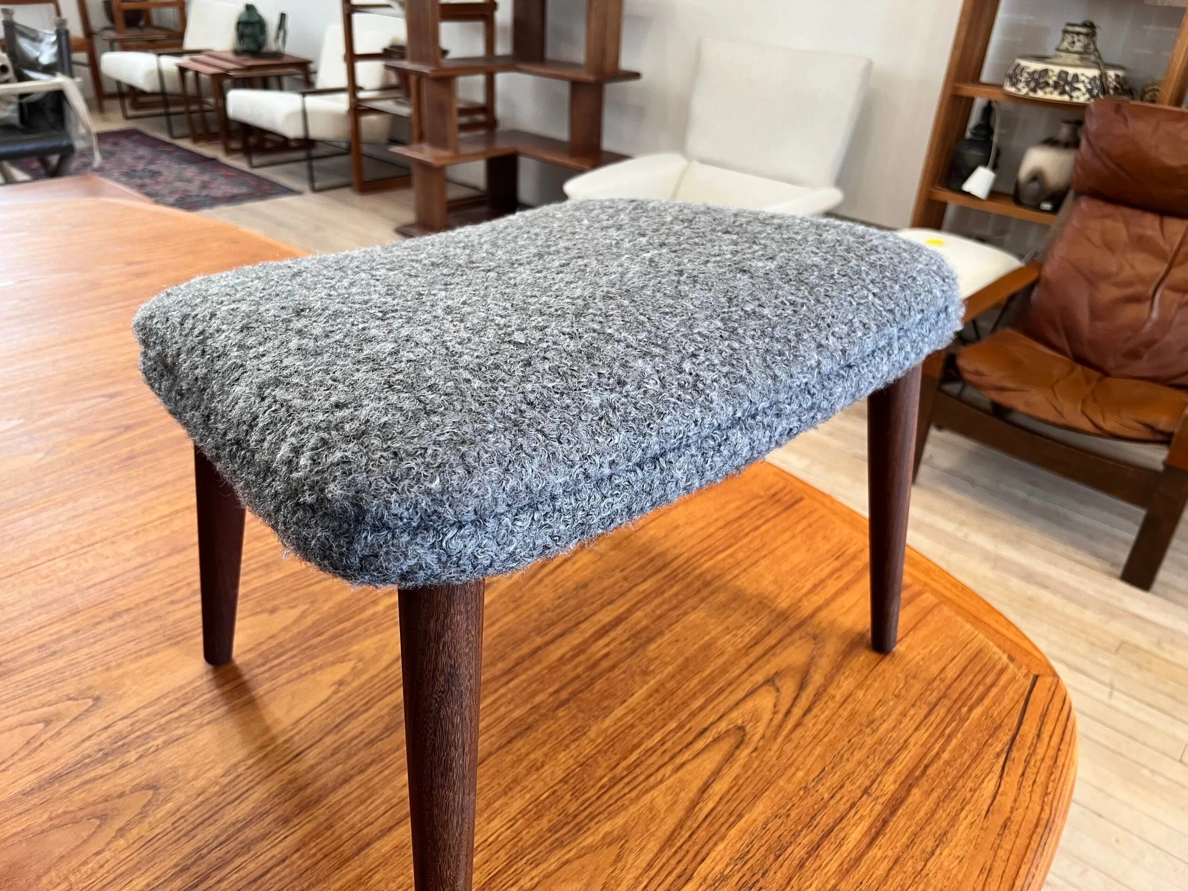 Gray bouclé ottoman reupholstered and displayed on a teak coffee table