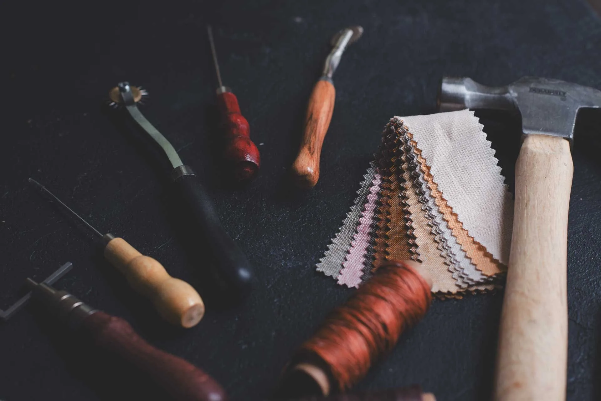 Upholstery hand tools and fabric swatches arranged on a dark workbench